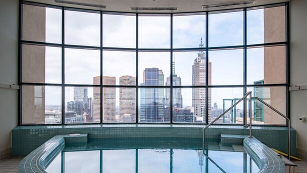 A modern indoor swimming pool with a panoramic city view through large windows. - Elegant 4B 2B Unit in Melbourne CBD w/ Parking! (Melbourne)