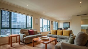 A spacious living room with large windows, a wooden coffee table, and a grey sofa set. - Elegant 4B 2B Unit in Melbourne CBD w/ Parking! (Melbourne)