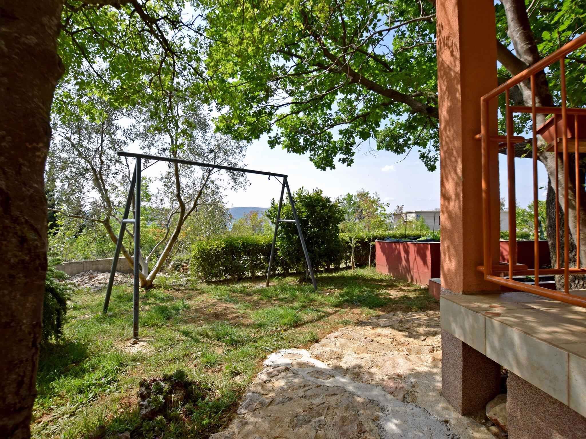 Un jardin avec une balançoire, un chemin de pierres et un bâtiment avec une porte rouge.