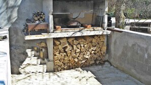 Una parrilla exterior con estructura de piedra, una chimenea y una pila de leña.