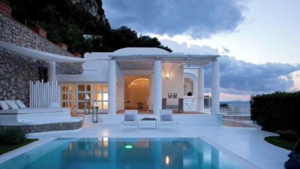 A modern poolside area with a clear view of the pool, a covered seating area, and a stone wall. - Villa Fortuna by MyVillaCollection (Capri)