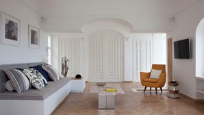 A spacious living room with a sofa, armchair, and coffee table. There are framed pictures on the wall, a television, and a door with decorative panels. - Villa Fortuna by MyVillaCollection (Capri)