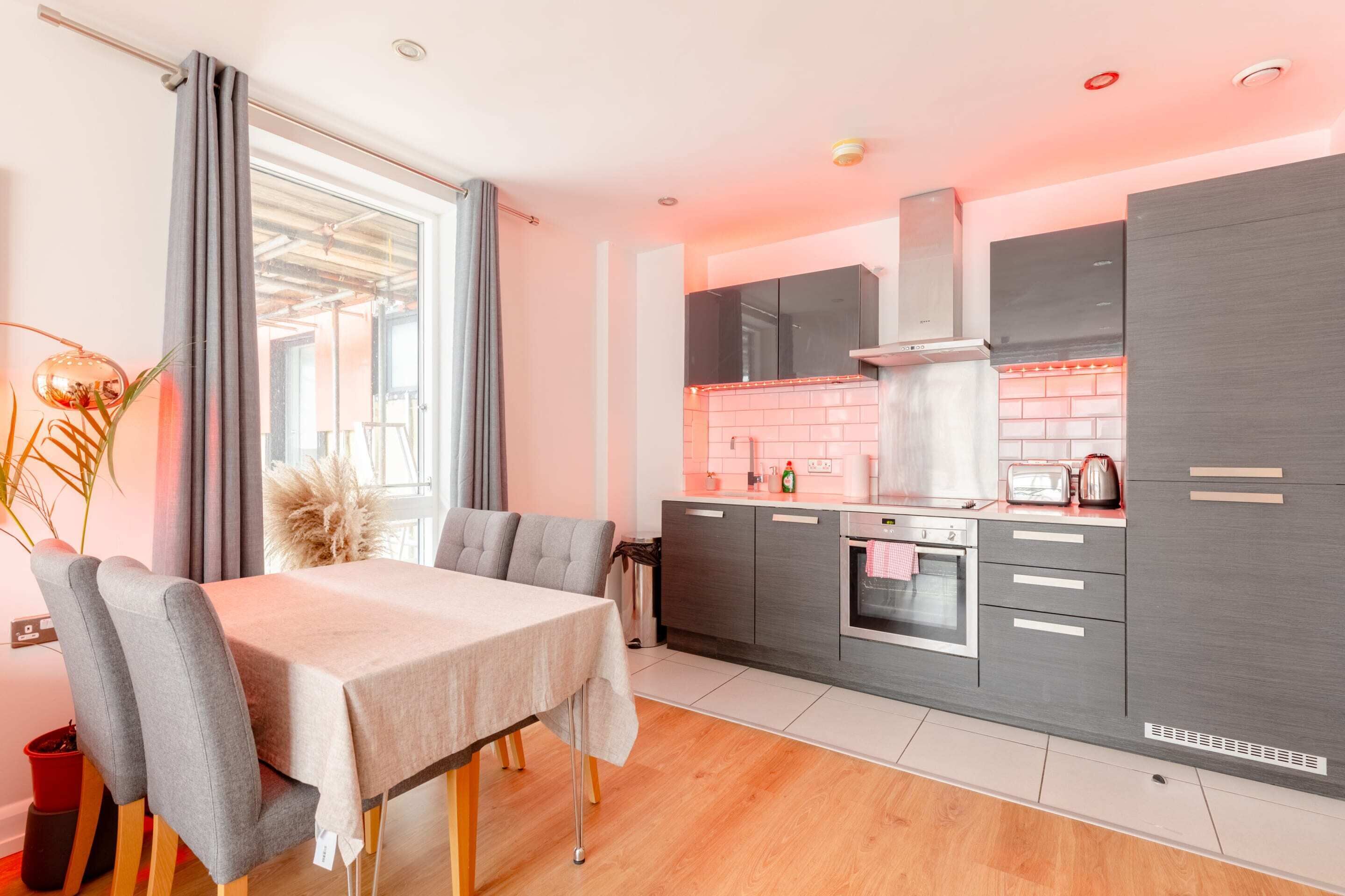 A modern kitchen with grey cabinets, a stainless steel range hood, and a pink-tiled backsplash.