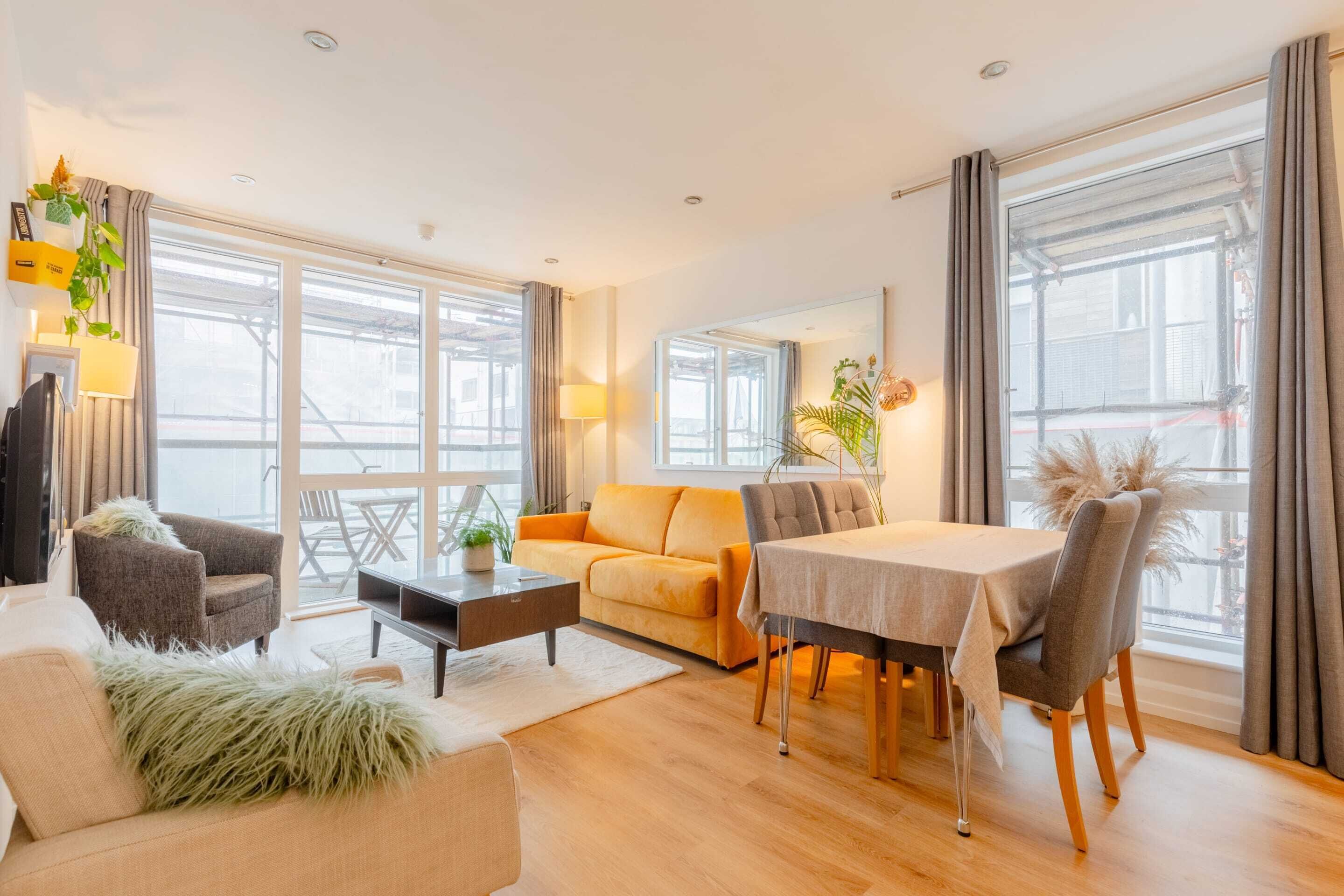 Ein modernes Wohnzimmer mit einer Couch, Sesseln, einem Esstisch und einem Balkon mit großen Fenstern.