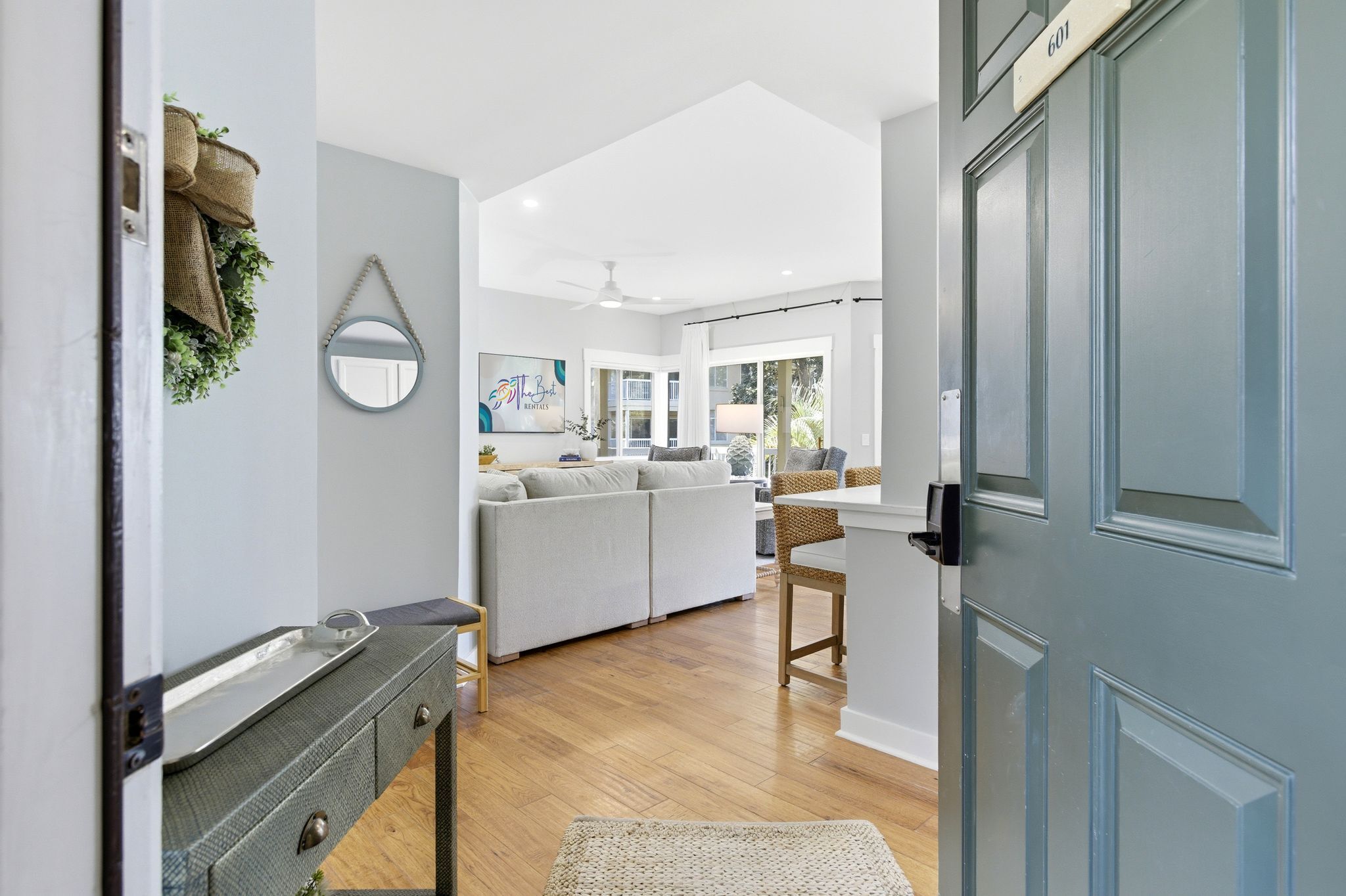 A modern interior with a grey door, a sofa set, a dining area, and a mirror on the wall.