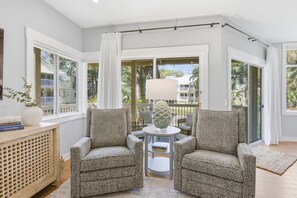 Una habitación con dos sillones, una mesita y un gran ventanal con cortinas.