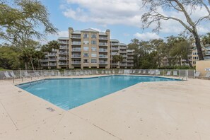 Une piscine avec des chaises longues, un bâtiment doté de nombreux balcons et des arbres environnants.