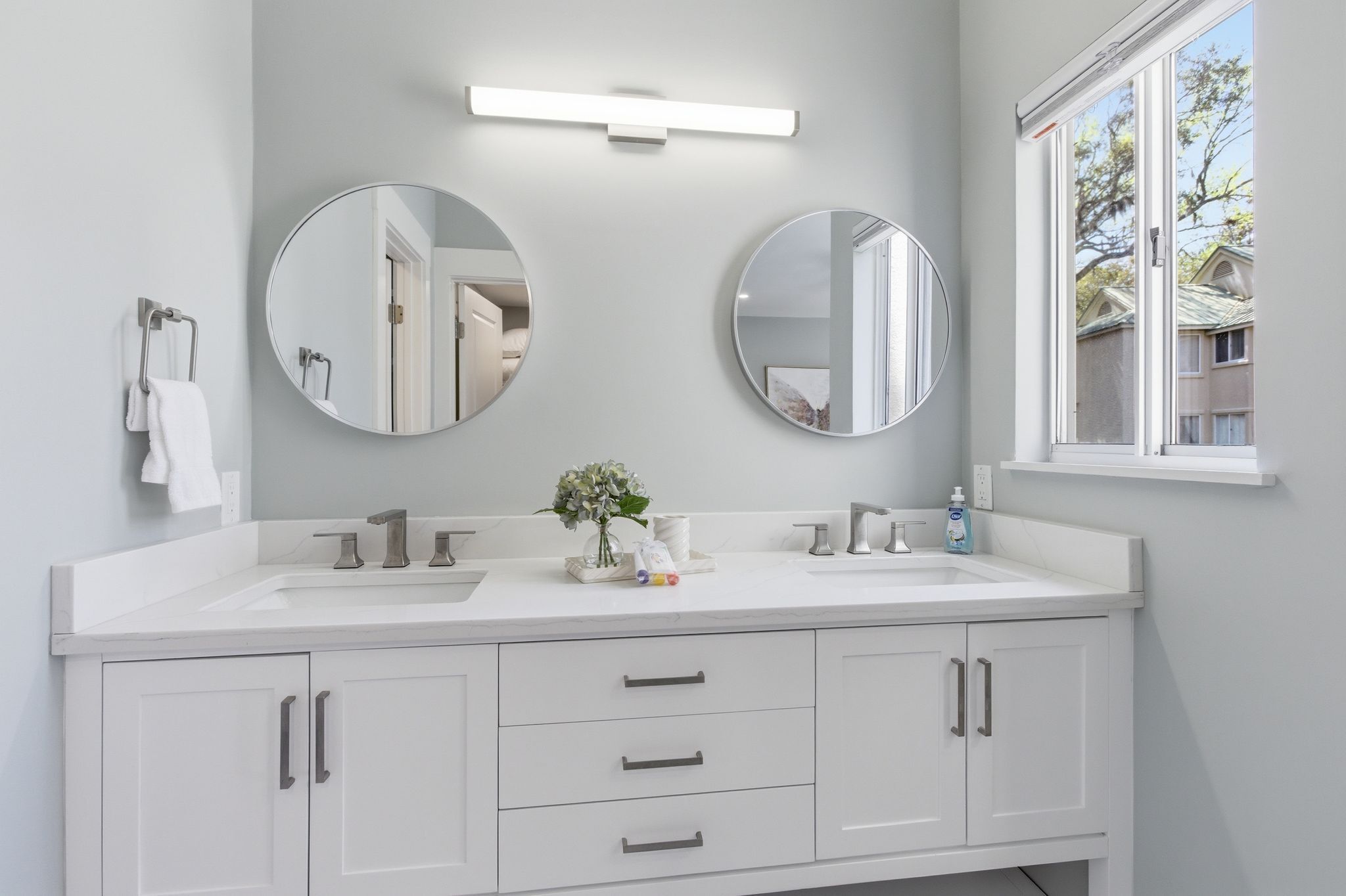 A bathroom with two sinks, a mirror, a towel rack, and a window.