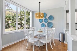 Un espace repas comprenant une table ronde, des chaises blanches, un luminaire suspendu et des œuvres d’art décoratives murales.