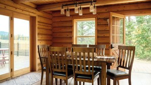 A wooden cabin with a dining table and chairs, large windows, and a view of the outdoors. - Black Bear Chalet - Alpine Falls Ranch (Superior)
