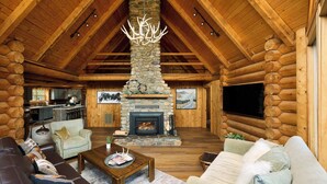 A log cabin interior with a stone fireplace, wooden ceiling, and a cozy seating area. - Black Bear Chalet - Alpine Falls Ranch (Superior)