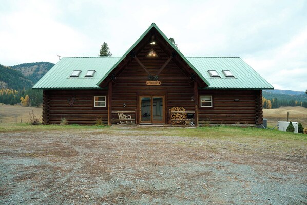 A rustic log cabin with a green metal roof, a front porch with a bench, and a sign that reads "Peace Bear Gulch." - Black Bear Chalet - Alpine Falls Ranch (Superior)