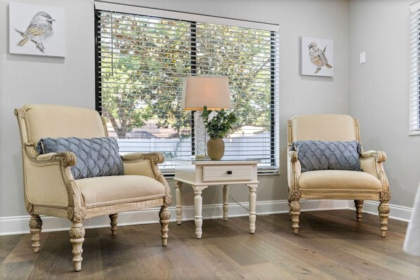 A room with two armchairs, a small table with a lamp, and artwork on the walls.