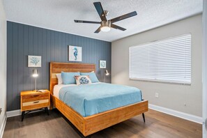 A bedroom with a wooden bed, a ceiling fan, wall-mounted lights, and a window with blinds.