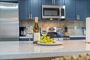A kitchen with a marble countertop, a bottle of wine, two glasses, and a plate of grapes.