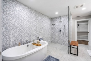 Ein modernes Badezimmer mit einer freistehenden Badewanne, einer Duschkabine aus Glas und einem kleinen Holzschemel.