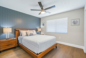 A bedroom with a wooden bed, two bedside tables, a ceiling fan, and a window with blinds. - Florida Haven 4/2.5 Vacation Ready Home! Book Now! (Seminole)