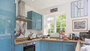 A modern kitchen with blue cabinets, a built-in oven, a window with a view of greenery, and a clock on the wall. - 4 bedroom accommodation in Rock (Rock)