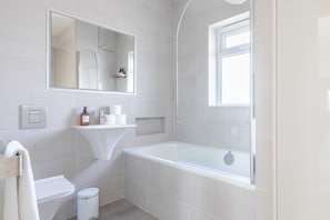 A modern bathroom with a bathtub, toilet, and sink. - Sleek Scandi-inspired 2BD Flat, Fulham (London)