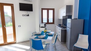 A modern kitchen with a dining area, a flat-screen TV mounted above the counter, and a window with a view. - Orizzonte Blu Superior 11, Palinuro, Cilento (Palinuro)
