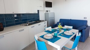 A modern kitchen with white cabinets, a blue tiled backsplash, and a dining area with a blue sofa and matching chairs.
