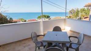 A balcony with a table and chairs, overlooking a coastal view.