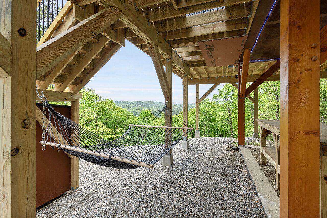 A wooden deck with a hammock and a bench, overlooking a forested landscape.