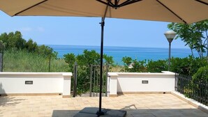 An outdoor patio with a large beige umbrella, a metal lamp post, and a view of the ocean. - Orizzonte Blu Deluxe 13 A, Palinuro, Cilento (Palinuro)