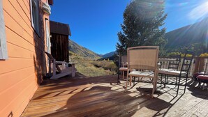 Une terrasse en bois avec des meubles d’extérieur, un bâtiment en bois et, au loin, un paysage montagneux.
