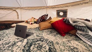 L’intérieur d’une tente, avec un ordinateur portable posé sur un tapis à motifs, des coussins et une couverture.