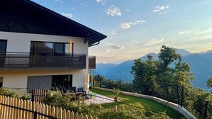 Una casa moderna de dos pisos con balcón, patio cercado y vista a la montaña.