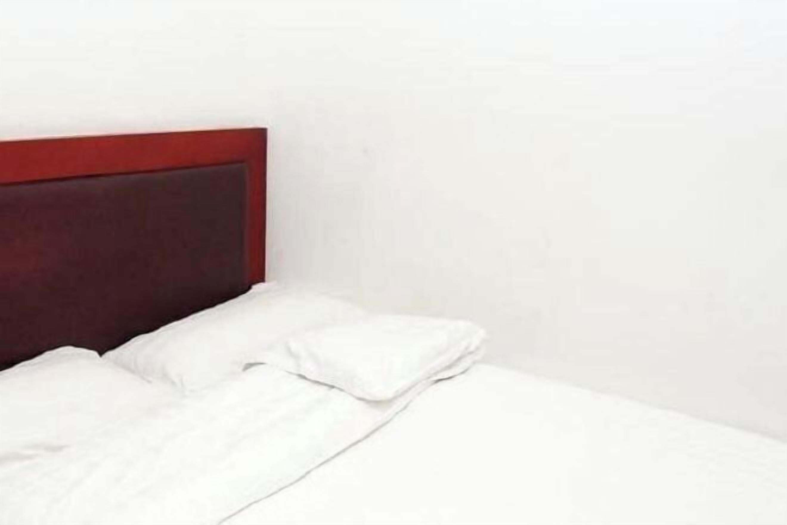 A bed with a wooden headboard, white bedding, and a plain wall.
