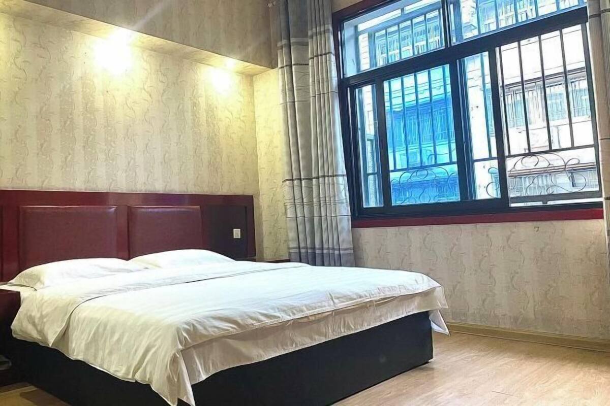 A bedroom with a bed, a window with curtains, and a wooden floor.