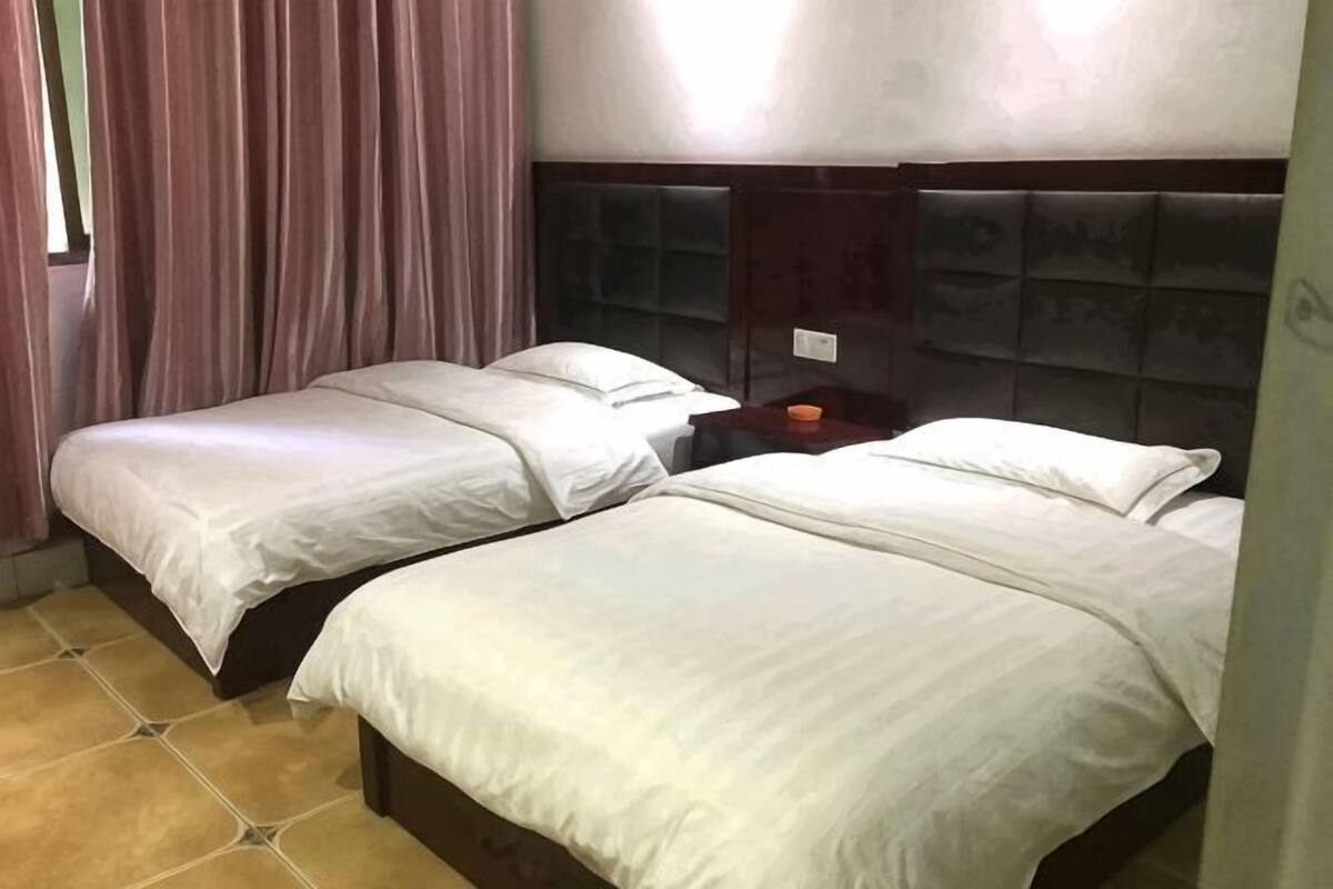 A hotel room with two beds, a nightstand, and a window with curtains.
