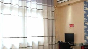 Une pièce avec un rideau à rayures, un téléviseur à écran plat fixé au mur, un bureau avec une chaise et un détecteur d’incendie rouge.