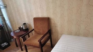 Une chambre d’hôtel avec une chaise en bois, une petite table avec une bouilloire et un lit recouvert d’une courtepointe à rayures.