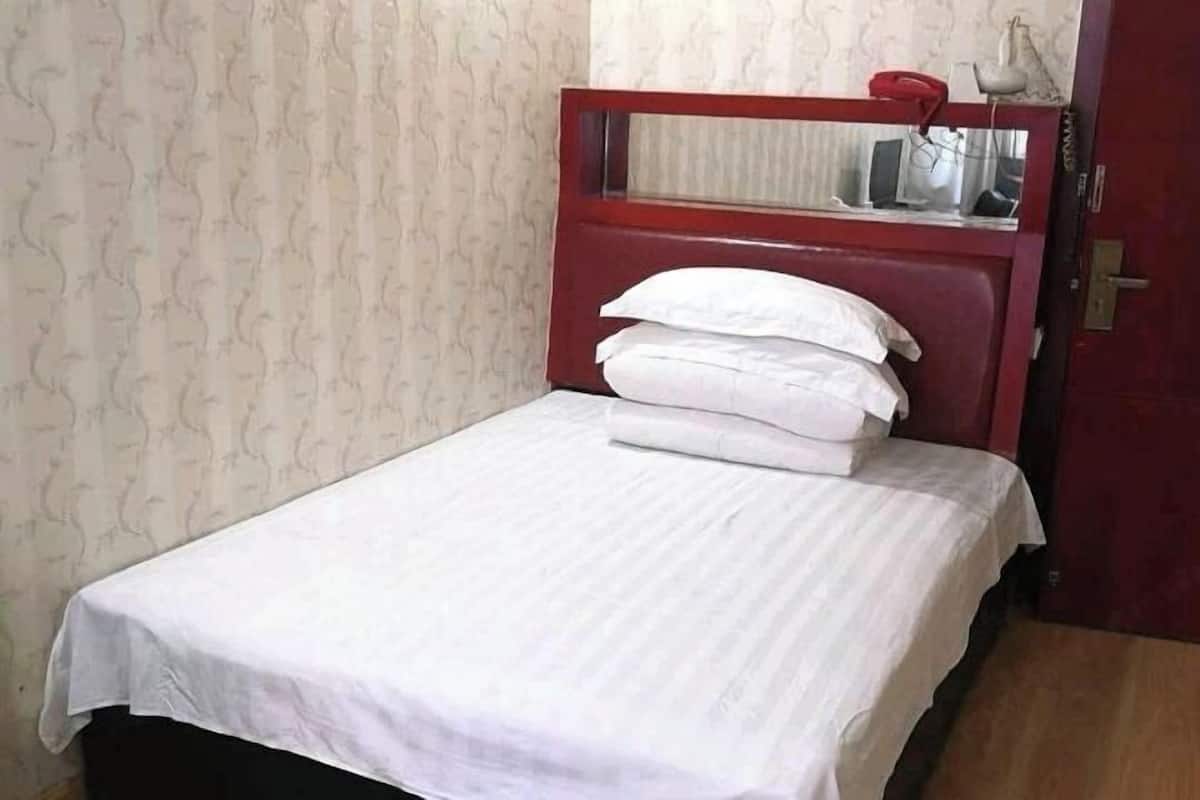 A small, single-bed room with a wooden headboard, white bedding, and a red door.