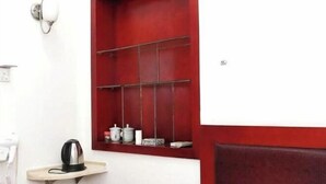Une fenêtre à cadre rouge avec des étagères, une bouilloire posée sur une petite table et un luminaire fixé au mur.