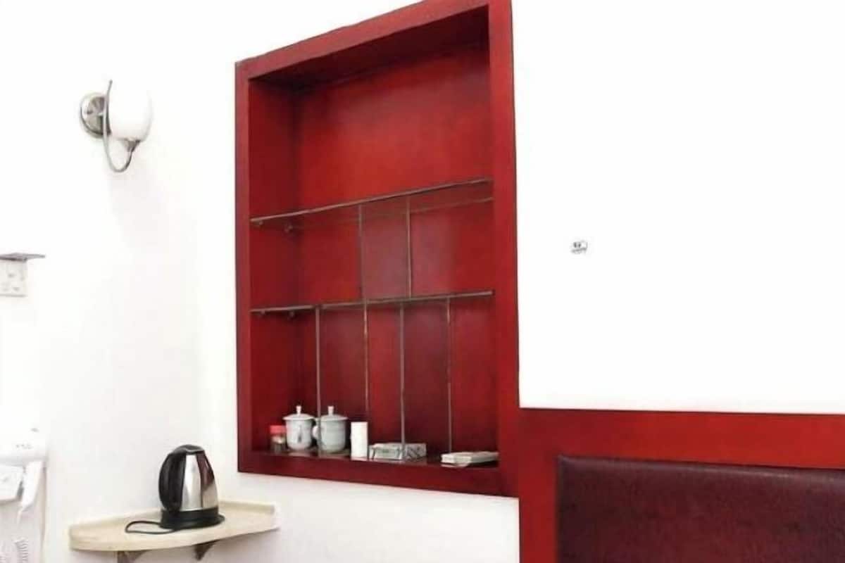 A red-framed window with shelves, a kettle on a small table, and a wall-mounted light fixture.