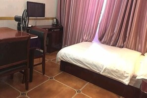 A hotel room with a bed, a desk, a chair, a television, and curtains.