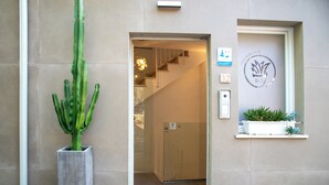 A hotel entrance with a cactus in a planter, a staircase leading to the interior, and a sign with the hotel's name and logo.
