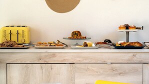 A kitchen counter with a yellow toaster, various pastries, and a bread roll.