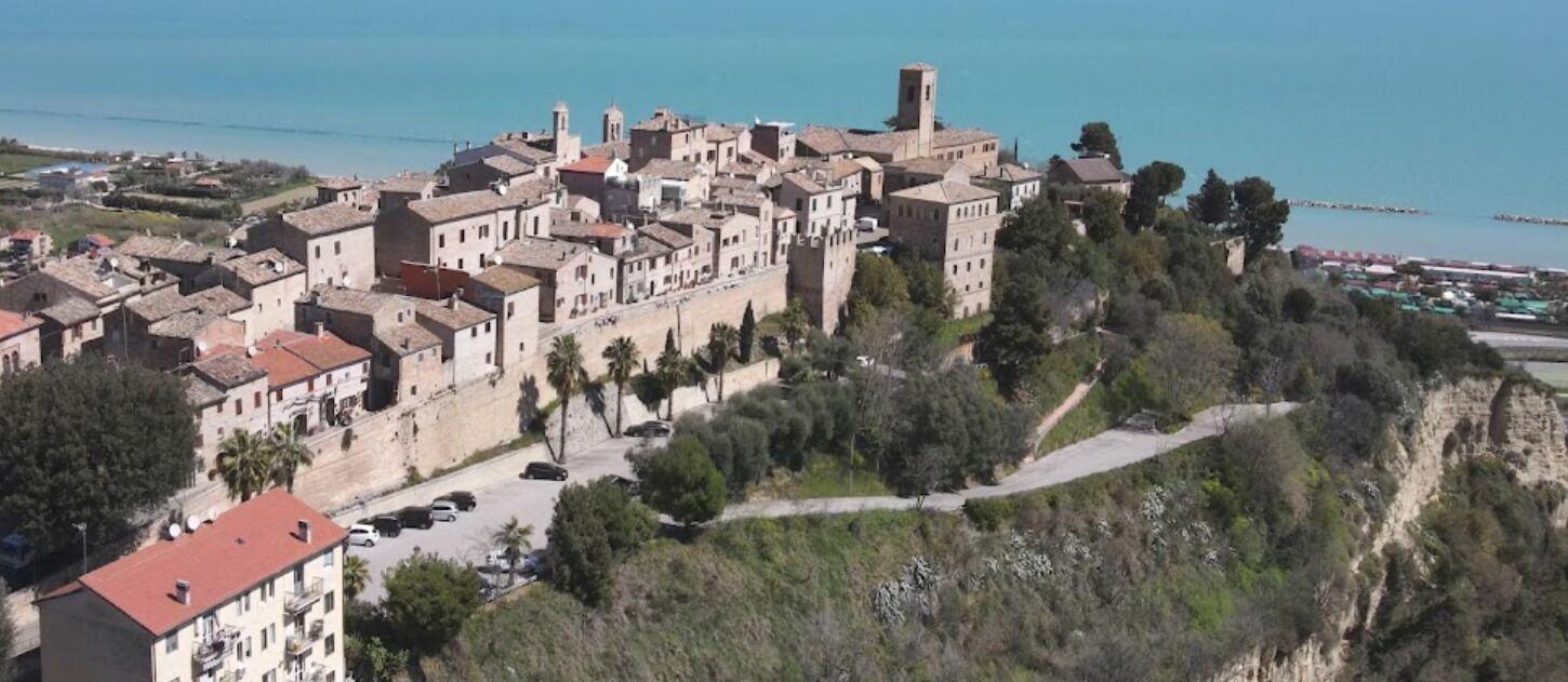A historic town with medieval architecture, a prominent tower, and a coastal backdrop.