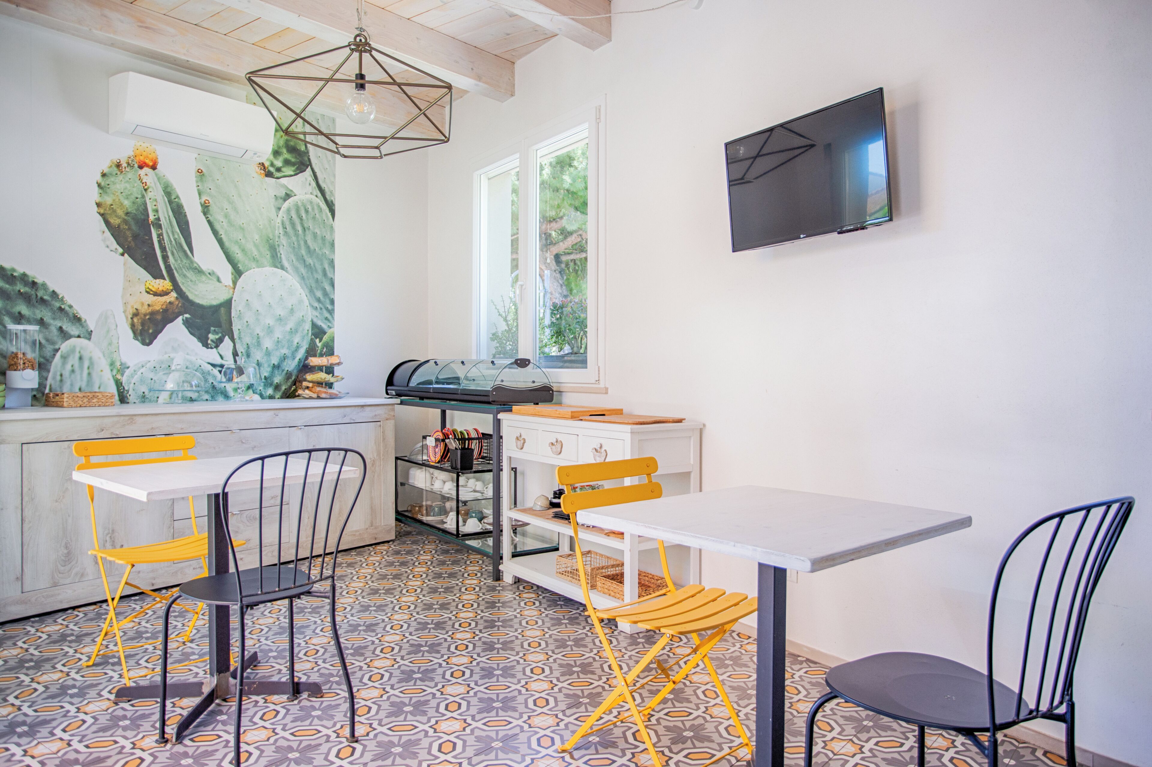 Une cuisine moderne ornée d’une fresque représentant des cactus, dotée d’un téléviseur à écran plat et comprenant un coin repas avec des chaises jaunes et noires.