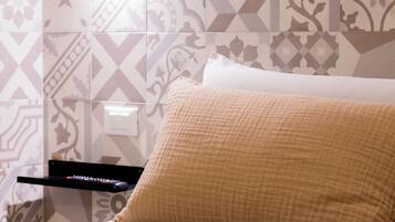 Una cama con un almohadón color crema y un control remoto sobre un pedestal negro.