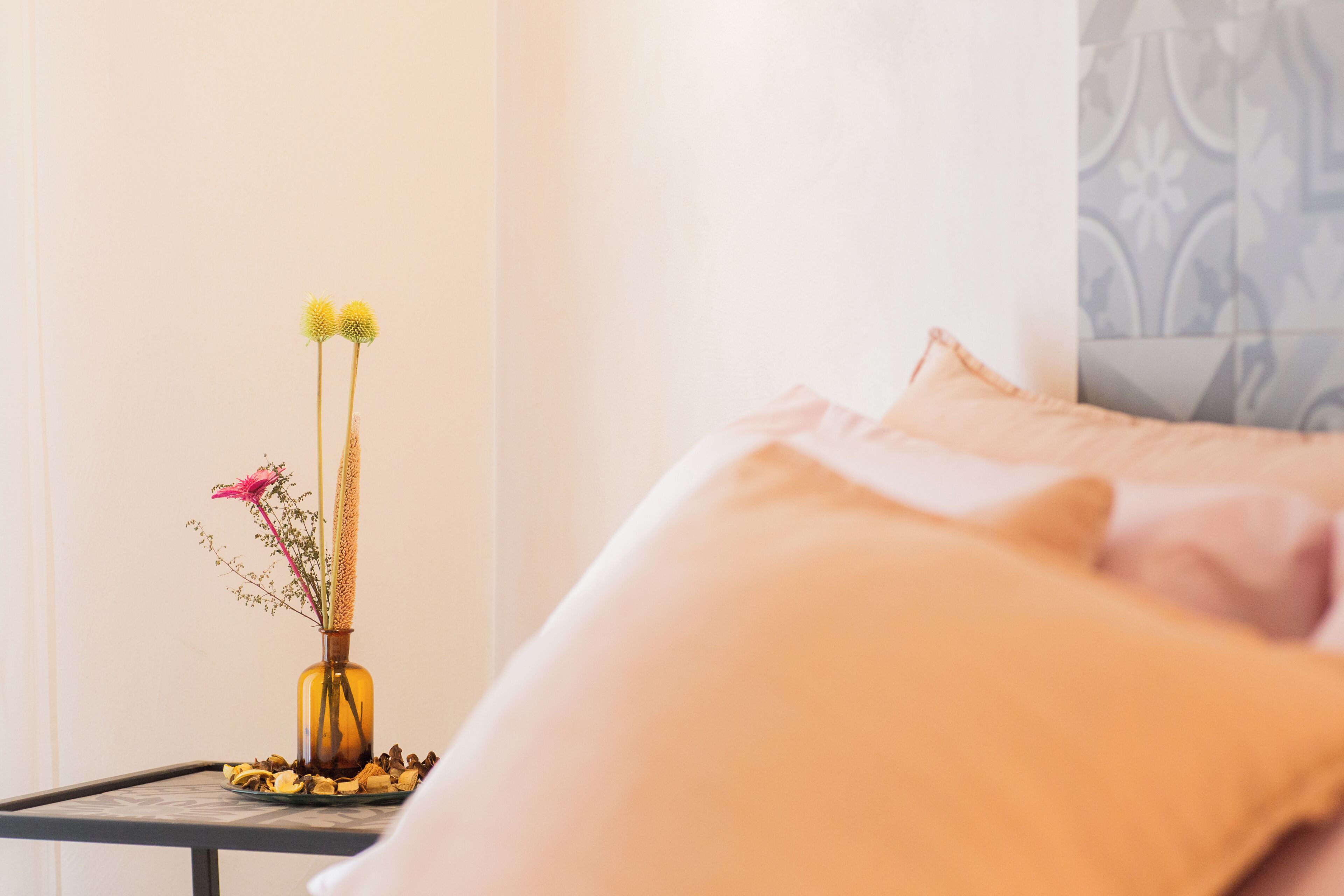 Ein Bett mit Kissen, ein Nachttisch mit Blumen in einer Vase und eine Wand mit Muster.