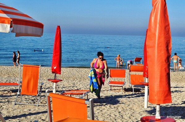A beach with orange chairs and umbrellas, a clear sky, and the sea in the background.