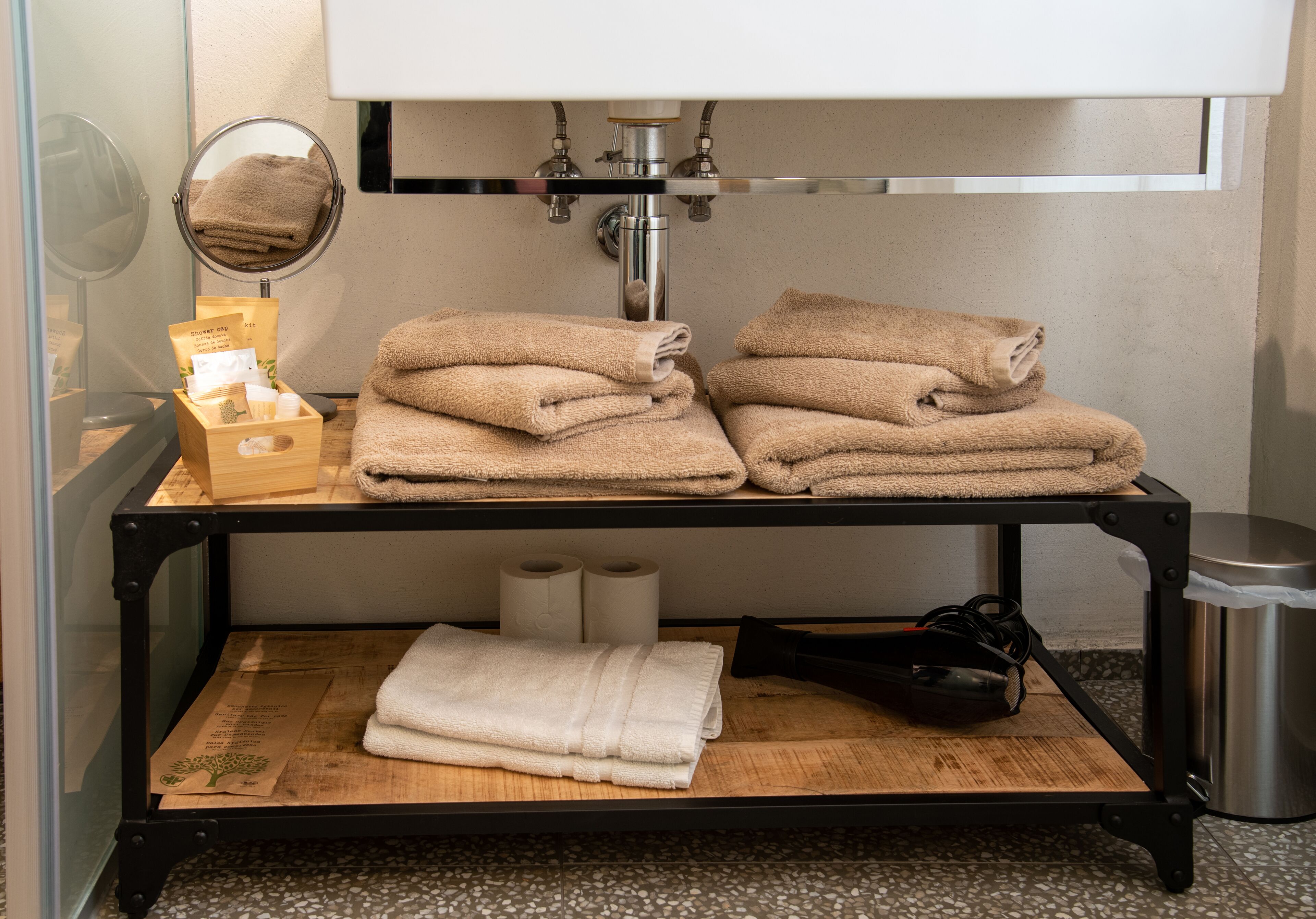 A bathroom with a shelf holding towels, a mirror, and toiletries.