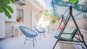 A patio with two blue chairs, a table, and a swing with a tropical pattern.
