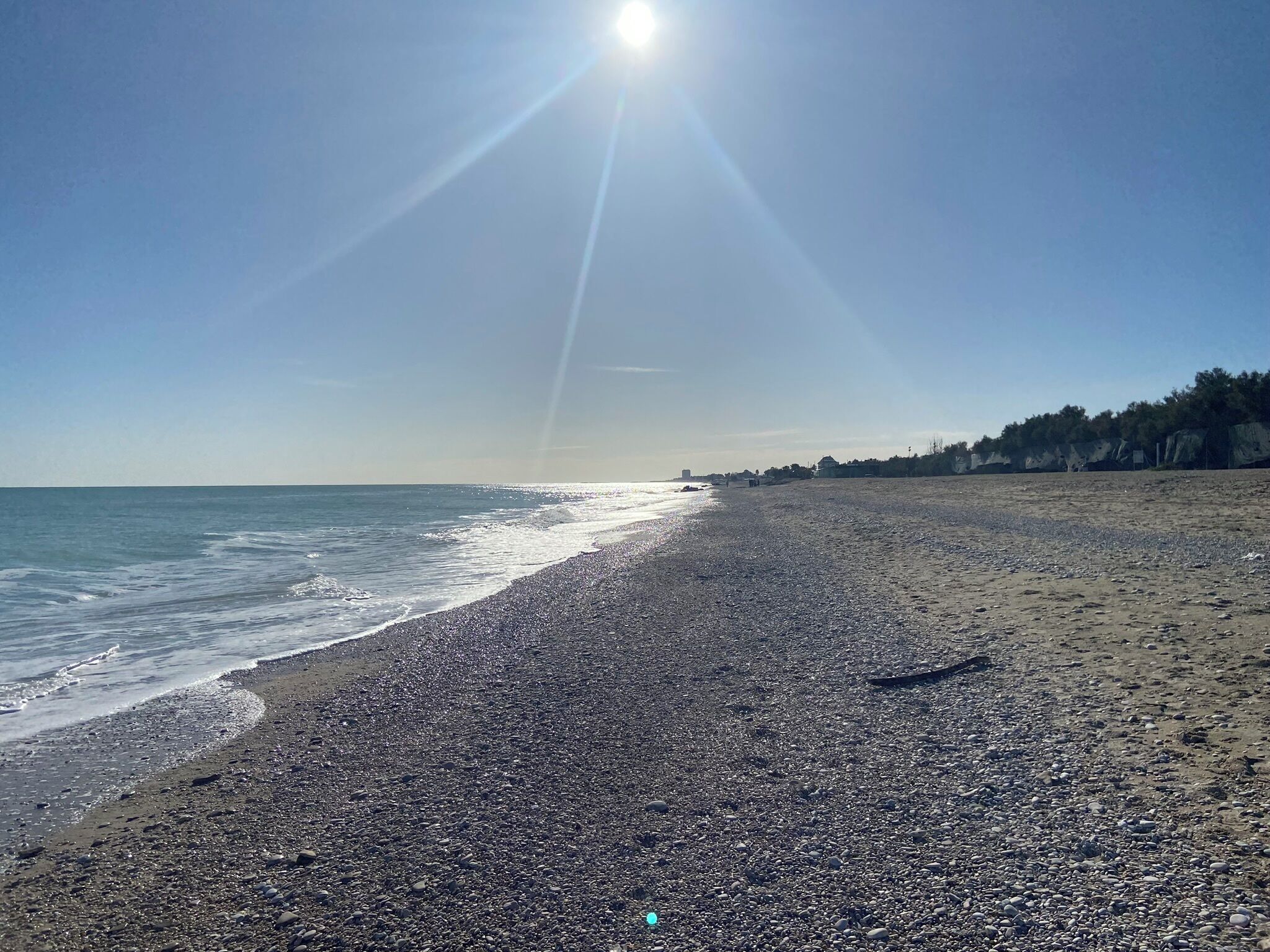 A pebbly beach with a clear sky and the sun shining.